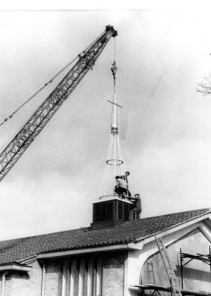 Rev'd Carlos standing far side of fleche when it was positioned on the roof, 1964.