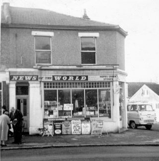 Our shop front, then called Hopes Green Stores.  My dad is standing outside talking to a customer. The dog is our little brown and white mongrel who was named Nicky. | Stephanie File